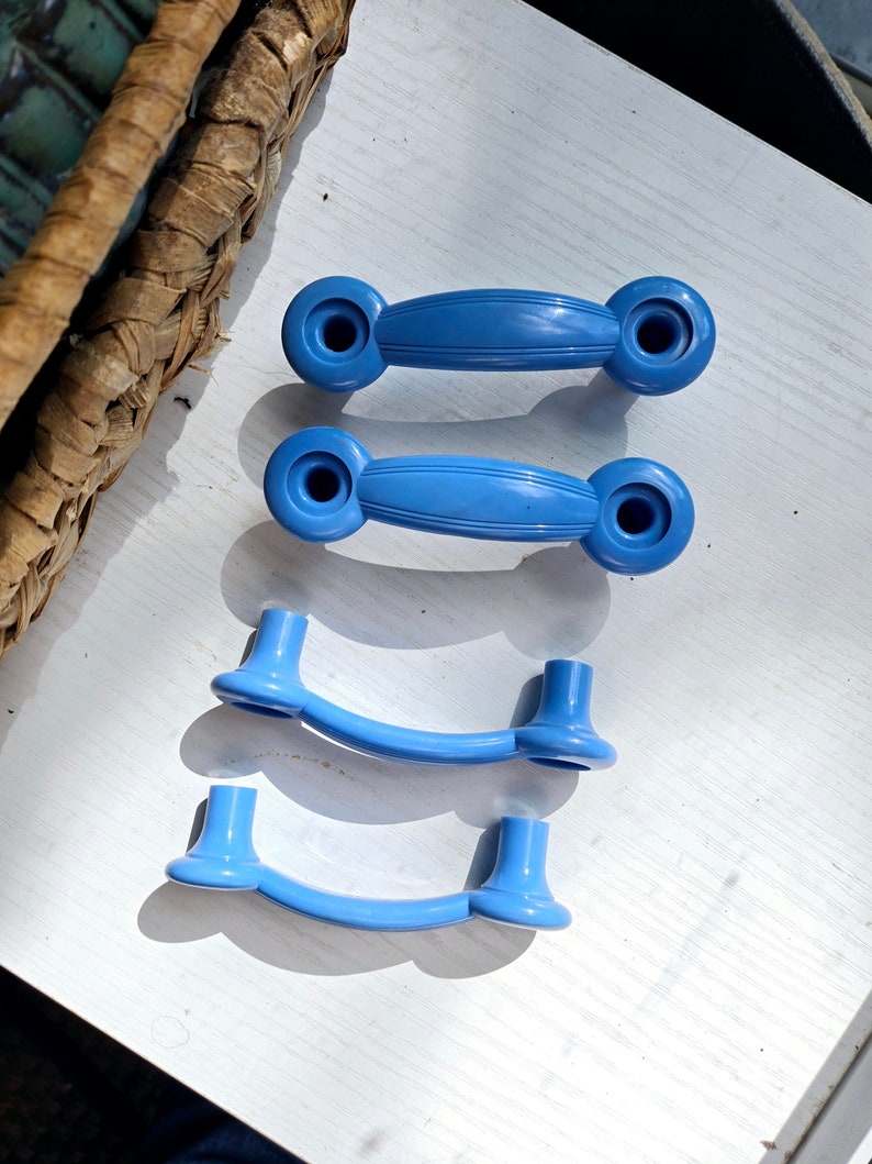 Puede incluir: Cuatro pomos de armario de pl&aacute;stico azul con un dise&ntilde;o redondeado y curvo. Los pomos est&aacute;n dispuestos en una pila vertical sobre una superficie blanca.