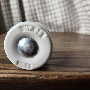 May include: A white ceramic knob with a silver center and the text "WP 361 USA" stamped on the side. The knob is set against a dark wood surface.