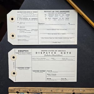 May include: Vintage postal ephemera featuring a receipt, dispatch note, and coupon. The documents, printed in black ink, include instructions, signature lines, and details for customs and delivery. A wooden ruler and pencil are also present.