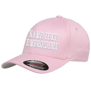 Puede incluir: Gorra de béisbol rosa con texto bordado en blanco que dice "NAME TEXT EMBROIDERY". La gorra tiene una etiqueta Flexfit negra y roja en la parte posterior.