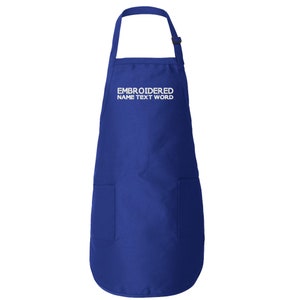 Puede incluir: Un delantal azul real con un bolsillo grande y una correa de cuello ajustable. El delantal tiene texto blanco que dice "EMBROIDERED NAME TEXT WORD".