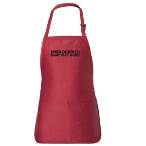 Puede incluir: Delantal de cocina rojo con un bolsillo grande y correas ajustables para el cuello. El delantal tiene texto bordado en negro que dice "EMBROIDERED NAME TEXT WORD".