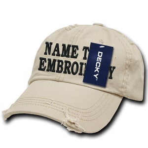 Może przedstawiać: Beżowa, zniszczona czapka z daszkiem z czarnym haftem, na którym widnieje napis "NAME TO EMBROIDERY". Do czapki przymocowana jest niebieska metka z napisem "DECKY".
