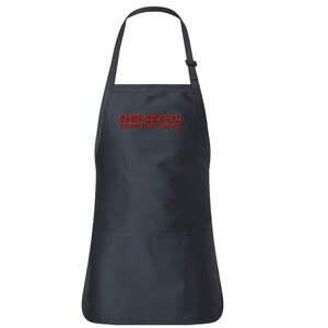 Puede incluir: Un delantal negro con un bolsillo grande en la parte delantera. El delantal tiene correas ajustables y está bordado con el texto "EMBROIDERED NAME TEXT WORD" en rojo.