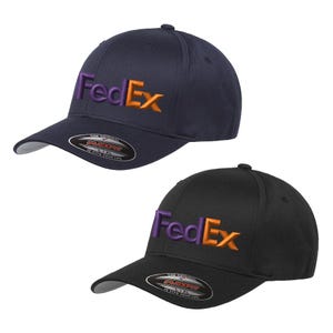 Puede incluir: Dos gorras de béisbol, una azul marino y otra negra, cada una con el logotipo de FedEx bordado en morado y naranja. Las gorras tienen una visera curva y una etiqueta Flexfit.