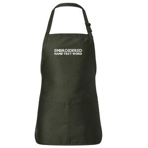 Puede incluir: Un delantal verde oscuro con un bolsillo grande en la parte delantera. El delantal tiene correas ajustables y el texto "EMBROIDERED NAME TEXT WORD" está bordado en blanco en la parte delantera.