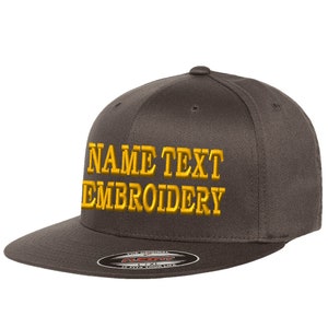 May include: A dark grey fitted baseball cap with gold embroidered text that reads "NAME TEXT EMBROIDERY".