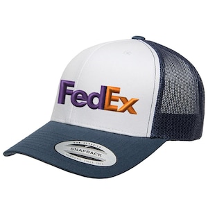 May include: A white and navy blue trucker hat with the FedEx logo embroidered on the front. The hat features a white front panel, a navy blue brim and mesh back, and the text "FedEx" in purple and orange.