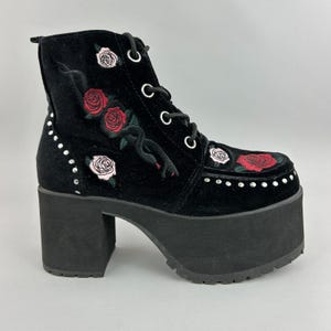 May include: Black platform ankle boot with embroidered red and pink roses, a black snake design, and silver studs. The boot has a lace-up closure and a chunky heel.