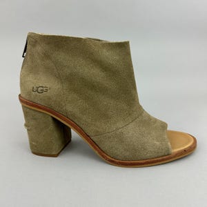 Könnte beinhalten: Offene Stiefeletten von UGG aus olivgrünem Wildleder. Die Stiefeletten haben einen Blockabsatz, einen Reißverschluss hinten und das UGG-Logo. Die Absatzhöhe beträgt ca. 7,6 cm.