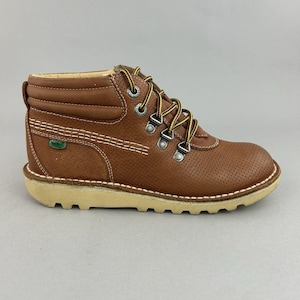 May include: Brown leather ankle boot with a perforated design, yellow laces, and a beige sole. The boot features metal eyelets and a stitched design along the side. A small green logo is visible on the side of the boot.