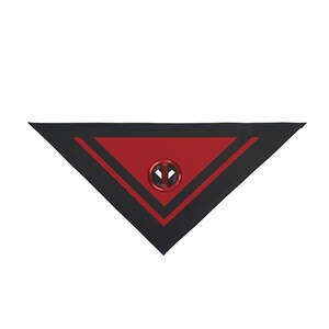 Puede incluir: Un accesorio triangular negro y rojo con el logotipo de Deadpool. El accesorio tiene un centro rojo con un patrón texturizado, un borde negro y rayas rojas. Un logotipo metálico de Deadpool está centrado.