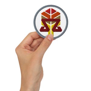 Może przedstawiać: Okrągła naszywka haftowana z szarym obramowaniem. Naszywka przedstawia stylizowany wzór drzewa z czerwonymi, pomarańczowymi i żółtymi liśćmi. Pień drzewa jest żółty, a gałęzie czerwone. Słowo "Sigma" jest wyszyte na czerwono pod drzewem.