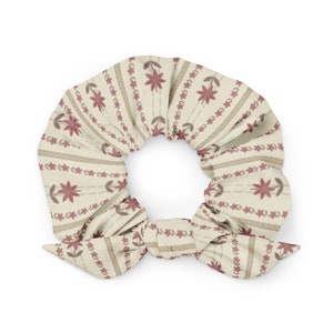 May include: A cream-colored scrunchie with a repeating pattern of small pink flowers and brown stems. The scrunchie is tied in a bow.