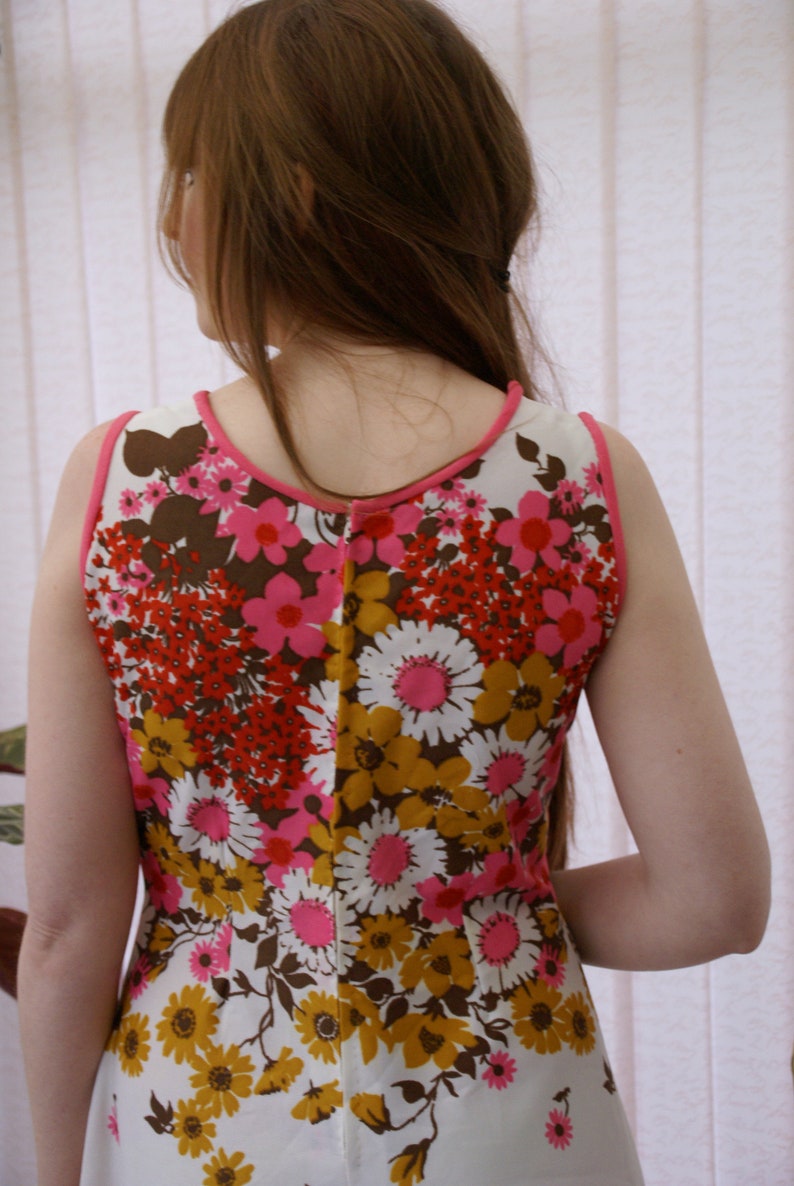 May include: A sleeveless dress with a white background and a floral pattern in shades of pink, red, brown, and yellow.