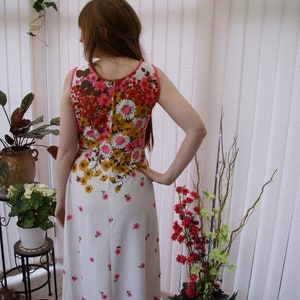 May include: A white maxi dress with a floral print in shades of pink, brown, and yellow. The dress has a sleeveless design and a fitted bodice.