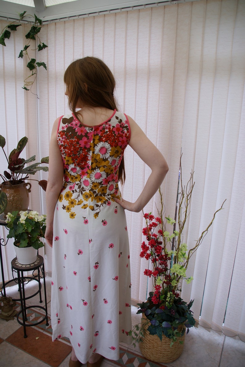 May include: A white maxi dress with a floral print in shades of pink, brown, and yellow. The dress has a sleeveless design and a fitted bodice.