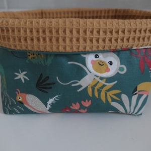 May include: A teal fabric storage basket with a brown waffle-textured top. The basket features a jungle-themed print with monkeys, toucans, and tropical plants.
