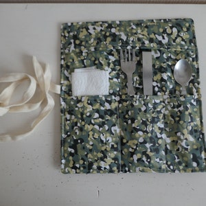 May include: A green and white patterned fabric roll-up utensil holder with a white cloth napkin, a fork, a knife, and a spoon.