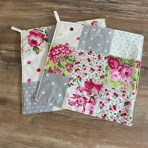 Peut inclure: Deux maniques patchwork à motifs floraux. L'une présente de grandes fleurs roses, tandis que l'autre mélange motifs floraux, pois et carrés gris avec des étoiles et des cœurs blancs. Chacune a une boucle blanche pour suspendre.