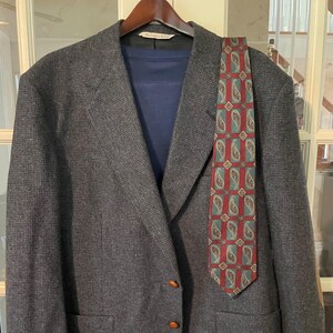 May include: A grey tweed blazer with a paisley patterned tie. The blazer has a single button closure and two pockets. The tie is red, green, and gold.