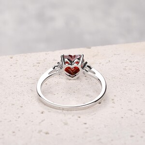 Puede incluir: Un anillo de plata con una piedra preciosa roja en forma de coraz&oacute;n y piedras preciosas m&aacute;s peque&ntilde;as y transparentes en la banda.