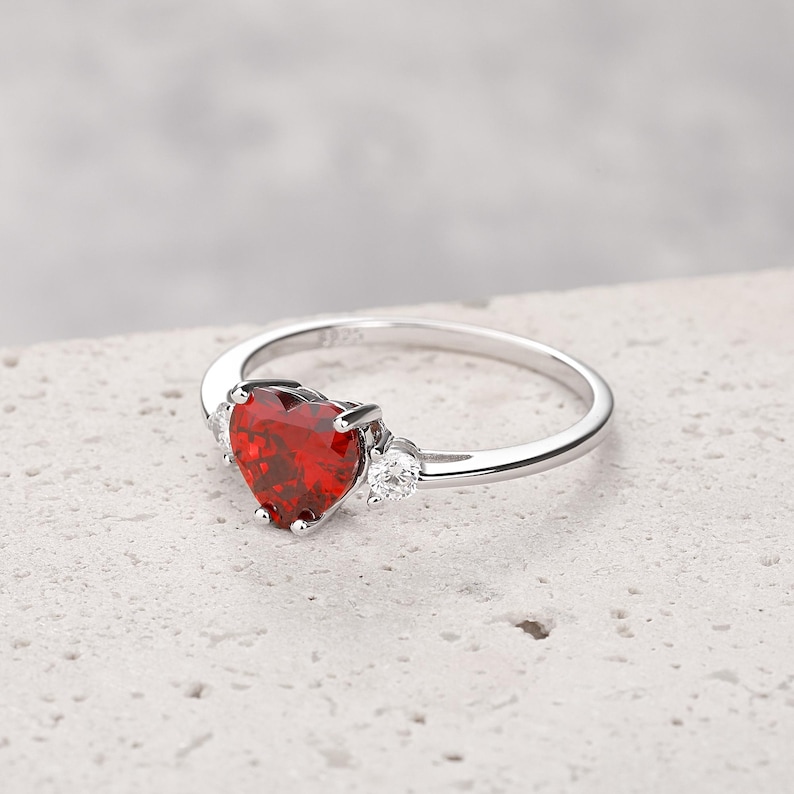 Puede incluir: Un anillo de plata con una gran piedra roja en forma de coraz&oacute;n y dos piedras peque&ntilde;as transparentes en la banda.