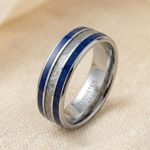 Könnte beinhalten: Ein Ring aus Wolframkarbid mit einem Mittelband aus kreuzschraffiertem Metall, flankiert von zwei tiefblauen Lapislazuli-Einlagen. Die Innenseite des Rings ist mit dem Text TUNGSTEN CARBIDE in einer klaren, serifenlosen Schrift graviert.