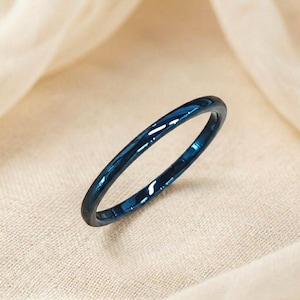 May include: A thin, dark teal ring with a glossy finish. The ring is a simple band design, with a smooth, reflective surface. The ring is set against a neutral, textured background.