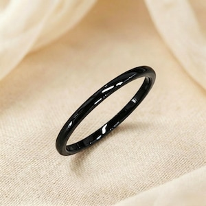 May include: A minimalist black ring with a high-shine finish. The ring is a simple band, reflecting light. The design is modern and understated. The ring is displayed on a neutral backdrop. This ring is suitable for everyday wear.
