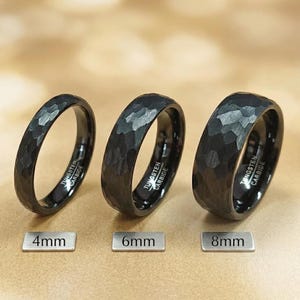 Puede incluir: Tres anillos de carburo de tungsteno negro con textura martillada. Los anillos se muestran en anchos de 4mm, 6mm y 8mm, con el texto "TUNGSTEN CARBIDE" grabado en el interior de cada banda. Cada anillo está acompañado por una etiqueta con su medida.