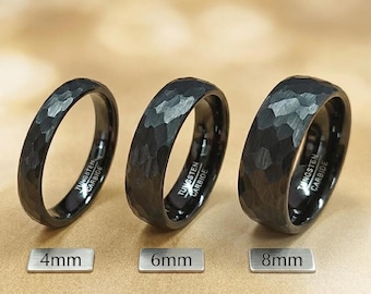 Könnte beinhalten: Drei schwarze Ringe aus Wolframkarbid mit gehämmerter Textur. Die Ringe sind mit Metallschildern versehen, die Breiten von 4mm, 6mm und 8mm anzeigen. Jeder Ring trägt die Gravur Tungsten Carbide auf der Innenseite.