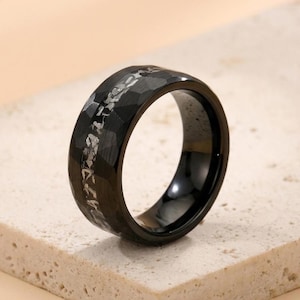 May include: A black ring with a hammered texture and a silver inlay. The ring has a polished, glossy finish on the inside. The band is approximately 0.3 inches wide.