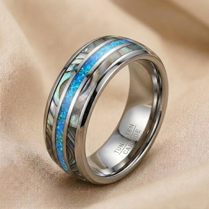 Peut inclure: Une bague en carbure de tungstène argenté avec une bande centrale d'opale bleu vif. La bague présente des incrustations de nacre irisée de chaque côté de l'opale, créant un contraste saisissant. C'est une pièce audacieuse.