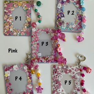 May include: Pink photo card holders with decorative borders and beaded keychains. Each holder features a different design, including puppies, bears, and other cute motifs. The keychains have heart-shaped clasps and colorful beads.