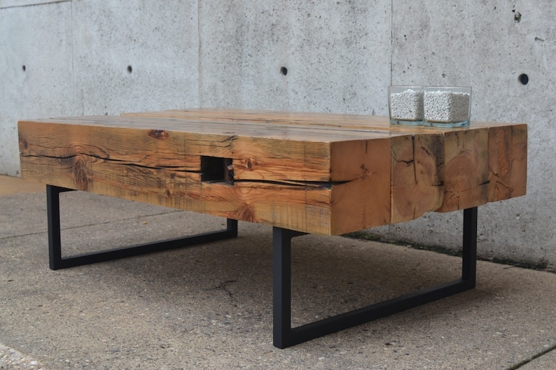 Pu&ograve; includere: Un tavolino da caff&egrave; in legno rustico con finitura in legno naturale e gambe in metallo nero. Il piano del tavolo ha un nodo ed &egrave; realizzato in legno riciclato.