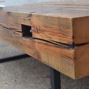 Pu&ograve; includere: Un tavolino da caff&egrave; in legno rustico con finitura in legno naturale e gambe in metallo nero. Il piano del tavolo ha un dettaglio unico di buco di nodo e un aspetto invecchiato.