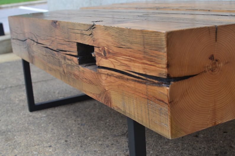 Pu&ograve; includere: Un tavolino da caff&egrave; in legno rustico con finitura in legno naturale e gambe in metallo nero. Il piano del tavolo ha un dettaglio unico di buco di nodo e un aspetto invecchiato.