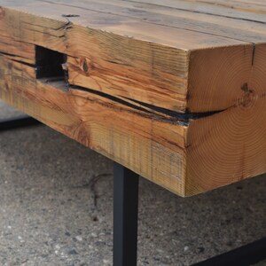 Pu&ograve; includere: Un tavolino da caff&egrave; in legno rustico con un piano spesso in legno riciclato e gambe in metallo nero. Il legno ha una finitura naturale invecchiata con nodi e motivi a venature.