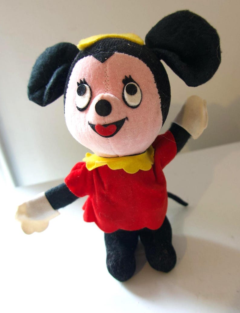 K&ouml;nnte beinhalten: Ein Vintage-Pl&uuml;schtier einer Zeichentrickfigur mit rosa Gesicht, schwarzen Ohren und einem gelben Hut. Die Figur tr&auml;gt ein rotes Kleid mit gelbem Kragen, schwarze Arme und Beine sowie wei&szlig;e Handschuhe. Das Spielzeug steht.