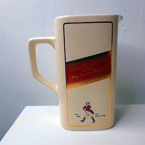 May include: Cream-colored ceramic pitcher with a rectangular label featuring the "Johnnie Walker Red Label Old Scotch Whisky" logo. The label has red and gold accents, and a small illustration of the Striding Man.