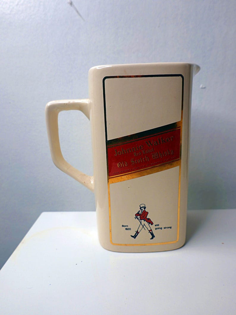 May include: Cream-colored ceramic pitcher with a rectangular label featuring the "Johnnie Walker Red Label Old Scotch Whisky" logo. The label has red and gold accents, and a small illustration of the Striding Man.
