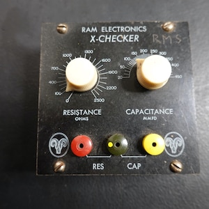 May include: A vintage RAM Electronics X-Checker RMS device. The black panel features white text, two cream-colored knobs, and input jacks in red, green, and yellow. The device measures resistance in ohms and capacitance in MMFD.