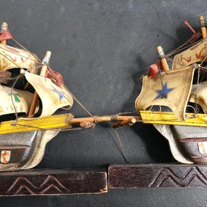 May include: Wooden bookends featuring two detailed ship models. The ships have cream-colored sails with red and blue accents, yellow decks, and gray hulls. The bookends are dark brown with carved details.