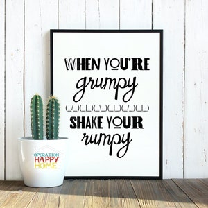 Puede incluir: Impresión enmarcada en blanco y negro con el texto "WHEN YOU'RE grumpy (___)_)_______)_______) SHAKE YOUR rumpy" sobre un fondo blanco. Una planta de cactus en maceta está en primer plano.