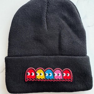 May include: Black knit beanie with a row of five embroidered Pac-Man ghosts in red, yellow, blue, pink, and red.
