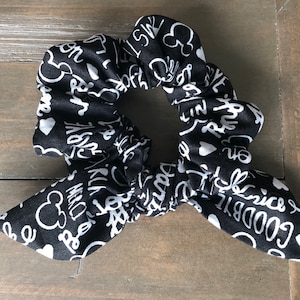 Puede incluir: Un scrunchie negro y blanco con un diseño de Mickey Mouse y texto blanco que dice "Good Time" y "Magic" en él.