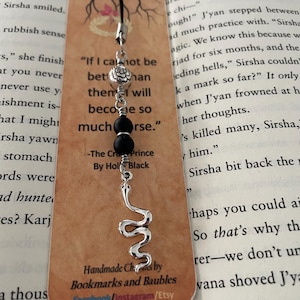 May include: A handmade bookmark with a black cord, a silver snake charm, and black beads. The bookmark has a brown tag with text from "The Cruel Prince" by Holly Black and the maker's name.
