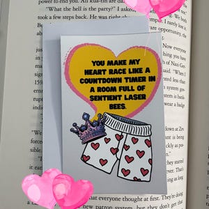 May include: A greeting card with a yellow heart and the text "YOU MAKE MY HEART RACE LIKE A COUNTDOWN TIMER IN A ROOM FULL OF SENTIENT LASER BEES." Below the text is an illustration of underwear with red hearts and a crown.