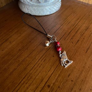 May include: A silver wolf charm with red beads and a gold bell on a black phone charm string.